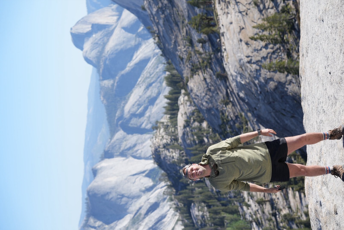 Christopher standing on a granite dome in Yosemite with Half Dome behind him